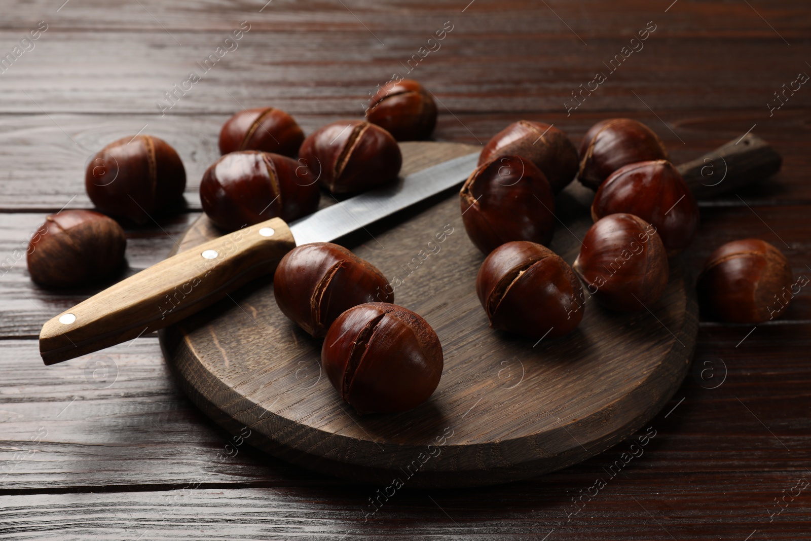 Photo of Roasted edible sweet chestnuts and knife on wooden table, closeup