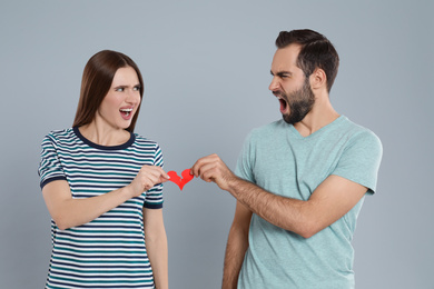 Photo of Couple tearing paper heart on light grey background. Relationship problems