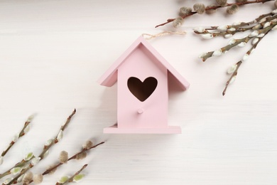 Photo of Beautiful bird house with heart shaped hole and willow branches on white wooden background. Spring flat lay composition