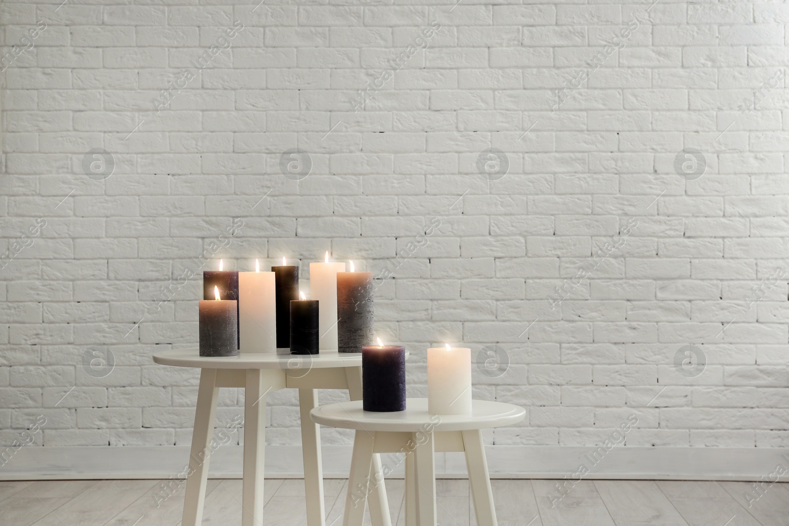 Photo of Burning candles on tables against brick wall with space for text