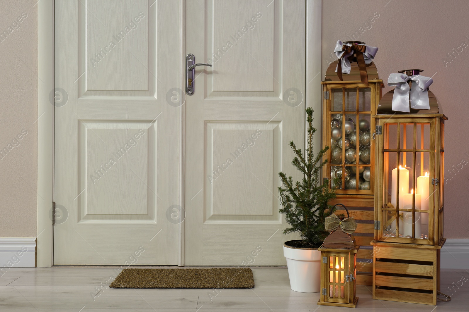 Photo of Beautiful Christmas lanterns and fir tree near entrance indoors