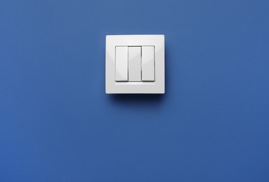 Photo of Modern plastic light switch on blue background. Space for text