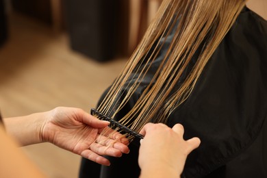 Photo of Professional hairdresser combing girl's hair in beauty salon, closeup