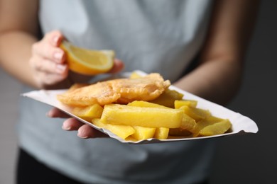 Photo of Woman adding lemon to delicious fish and chips on gray background, closeup