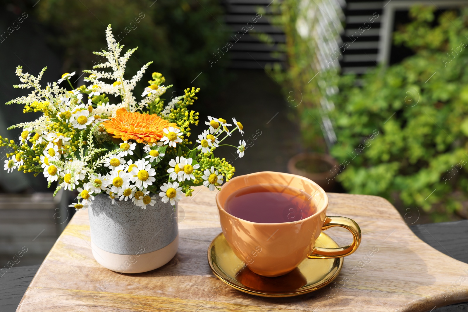 Photo of Cup of delicious chamomile tea and fresh flowers outdoors on sunny day