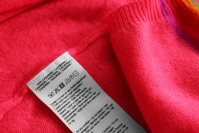 Photo of Clothing label in different languages on pink garment, closeup