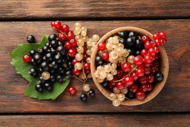 Different fresh ripe currants and green leaf on wooden table, flat lay
