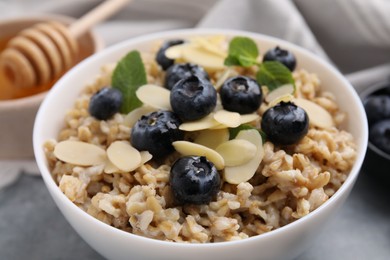 Photo of Tasty oatmeal with blueberries, mint and almond petals in bowl on grey table, closeup