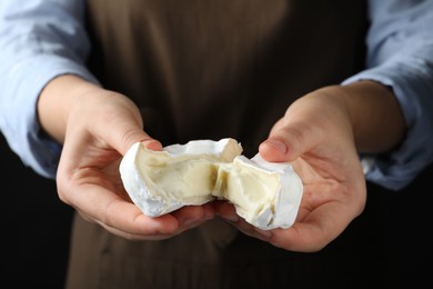 Photo of Woman breaking delicious brie cheese on black background, closeup