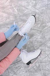 Woman lacing figure skates on ice, top view