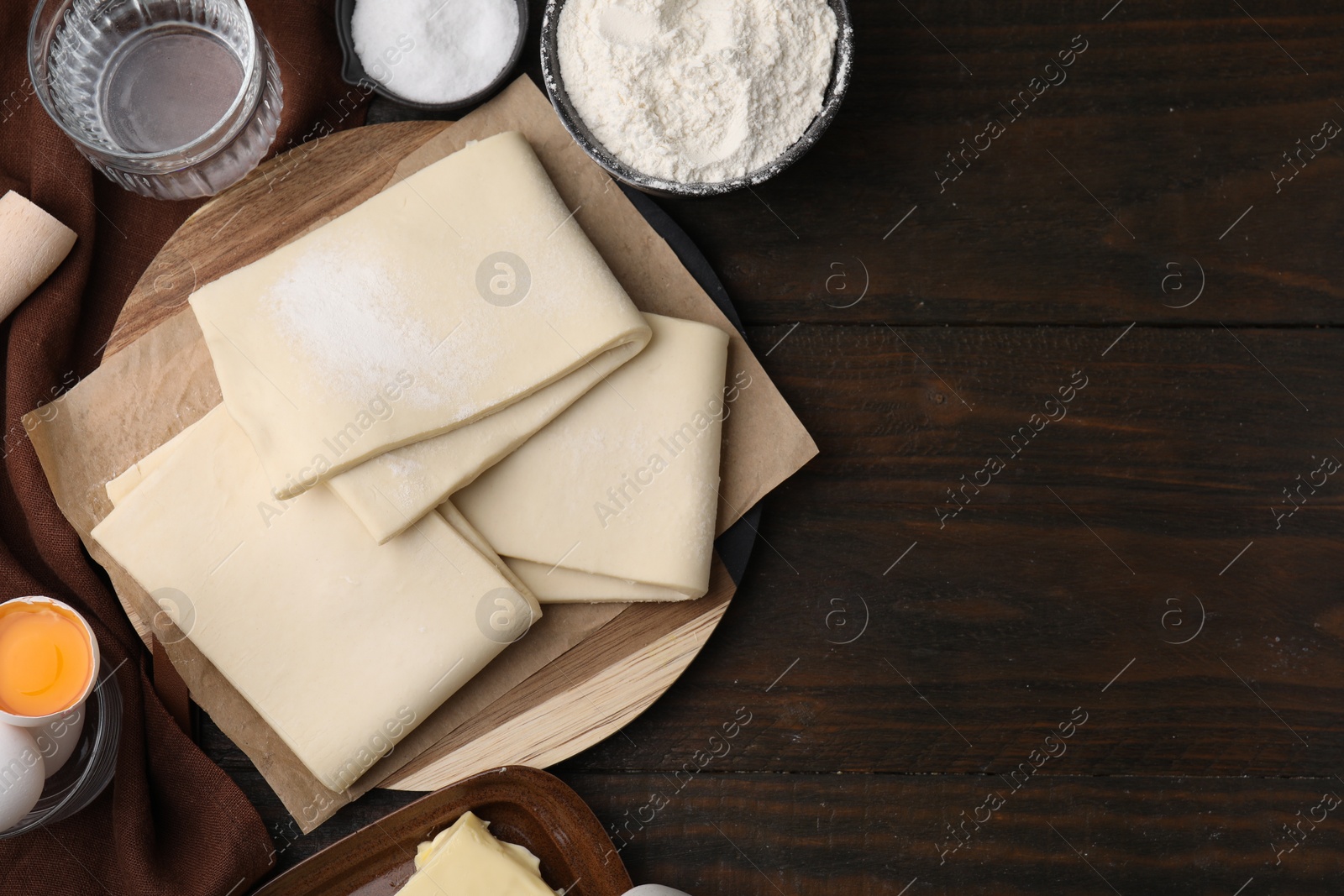 Photo of Raw puff pastry dough and ingredients on wooden table, flat lay. Space for text