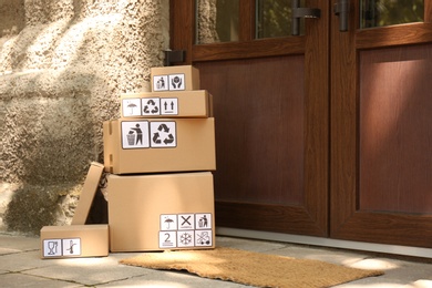 Photo of Cardboard boxes with different packaging symbols near entrance, space for text. Parcel delivery