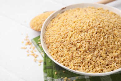 Raw bulgur in bowl on white table, closeup