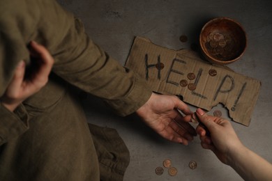 Photo of Woman giving coins to homeless, closeup. Help sign and bowl with donations on cement, top view