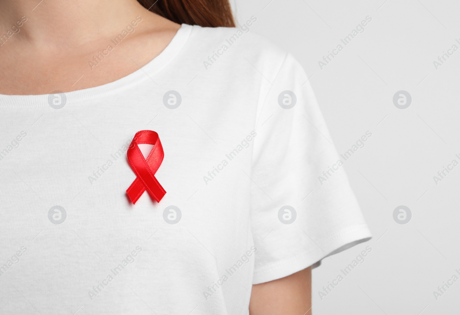 Photo of Woman with red ribbon on t-shirt against light background. Cancer awareness