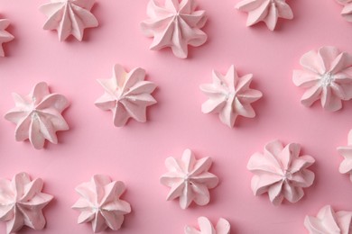 Many tasty meringue cookies on pink background, flat lay