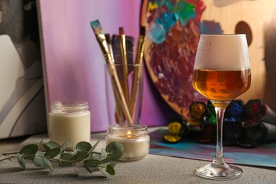 Brushes with colorful paints, candles and glass of wine on light gray table