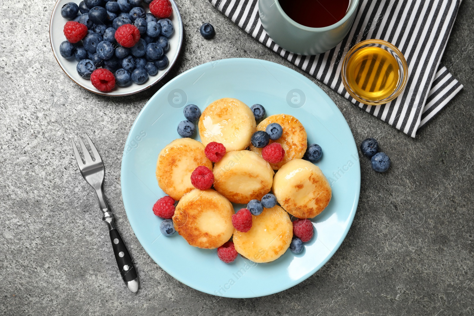 Photo of Delicious cottage cheese pancakes with fresh berries and honey on grey table, flat lay