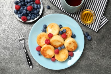 Delicious cottage cheese pancakes with fresh berries and honey on grey table, flat lay