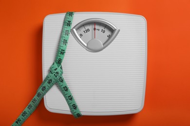 Photo of Scales and measuring tape on orange background, top view. Weight loss concept