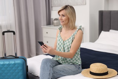 Photo of Smiling guest with smartphone relaxing on bed in stylish hotel room