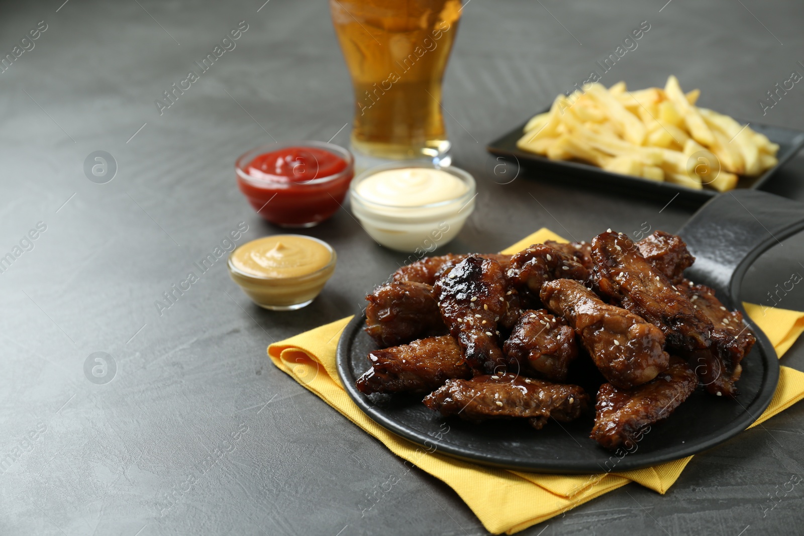 Photo of Tasty roasted chicken wings, sauces, french fries and glass of beer on black table. Space for text