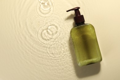 Bottle of face cleansing product in water against beige background, top view. Space for text