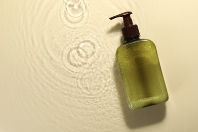 Photo of Bottle of face cleansing product in water against beige background, top view. Space for text