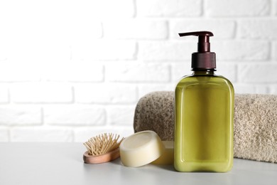 Bottle of shampoo, terry towel and wooden brush on white table, space for text