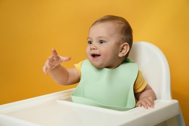Photo of Cute little baby wearing bib in highchair on yellow background