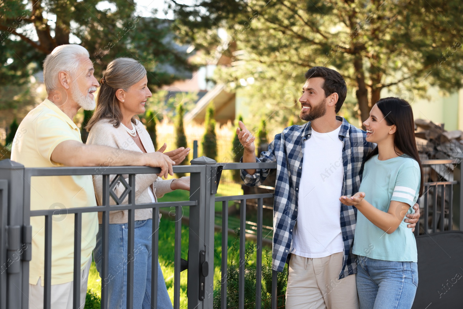 Photo of Friendly relationship with neighbours. Young family talking to elderly couple near fence outdoors