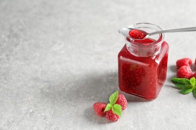 Glass jar and spoon of sweet jam with ripe raspberries on table. Space for text