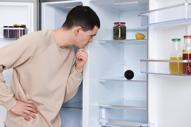 Thoughtful man near empty refrigerator in kitchen