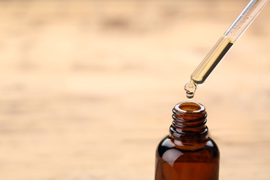 Photo of Dripping essential oil into glass bottle on wooden background, closeup. Space for text