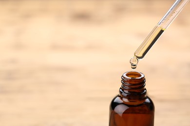 Dripping essential oil into glass bottle on wooden background, closeup. Space for text