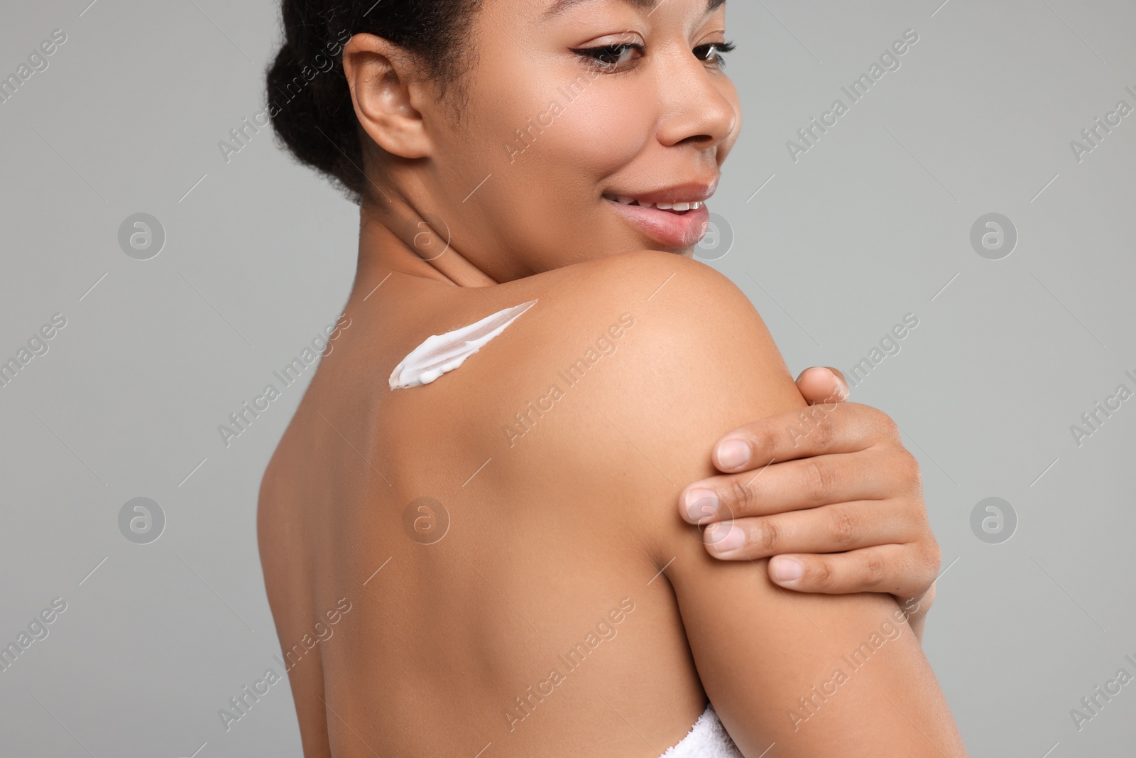 Photo of Young woman applying body cream onto back on grey background, closeup
