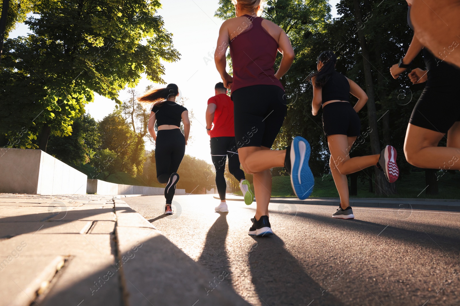 Photo of Group of people running outdoors on sunny day, back view