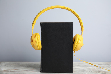 Book and modern headphones on white wooden table