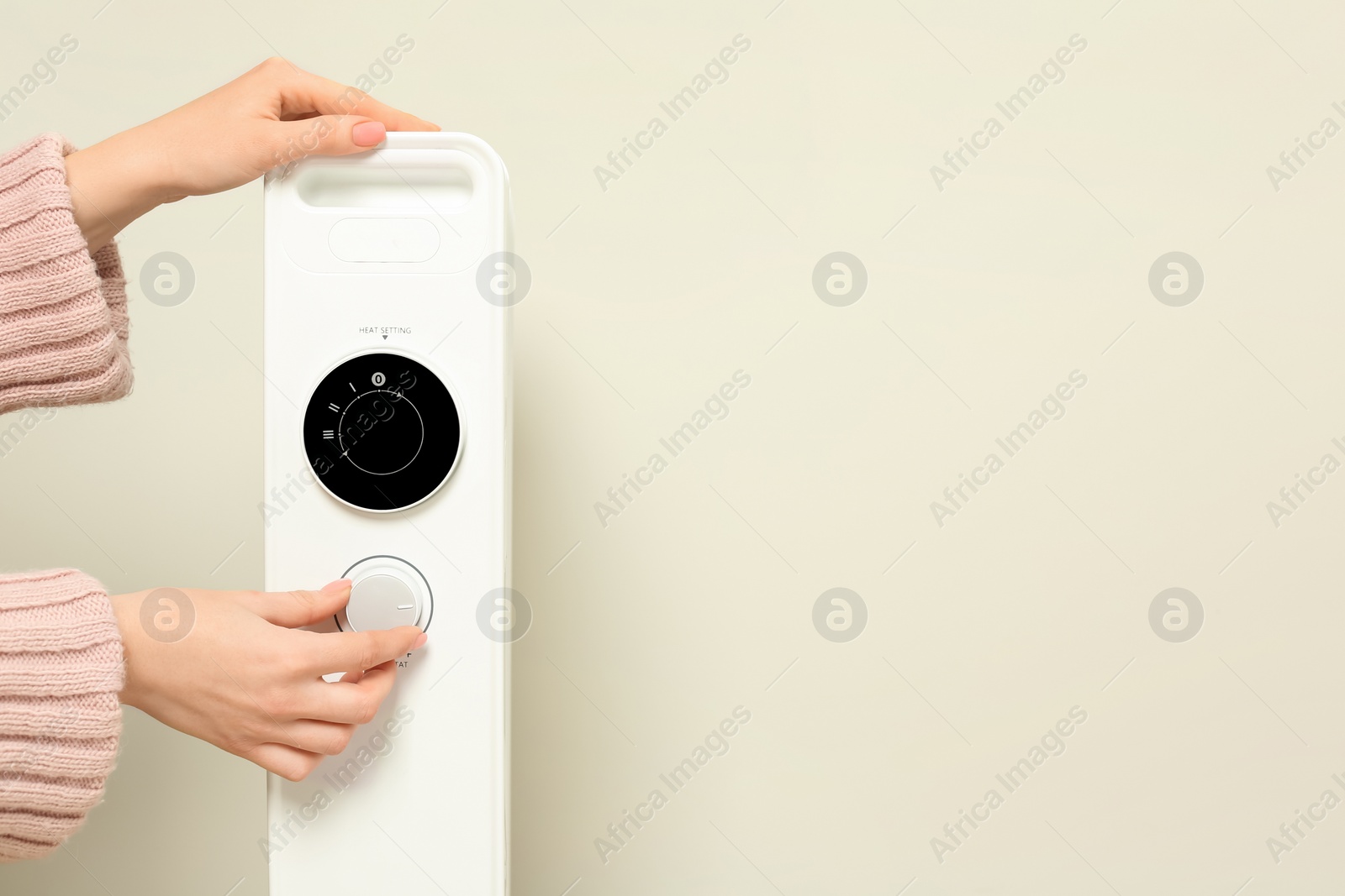 Photo of Young woman adjusting temperature on modern electric heater near beige wall, closeup. Space for text