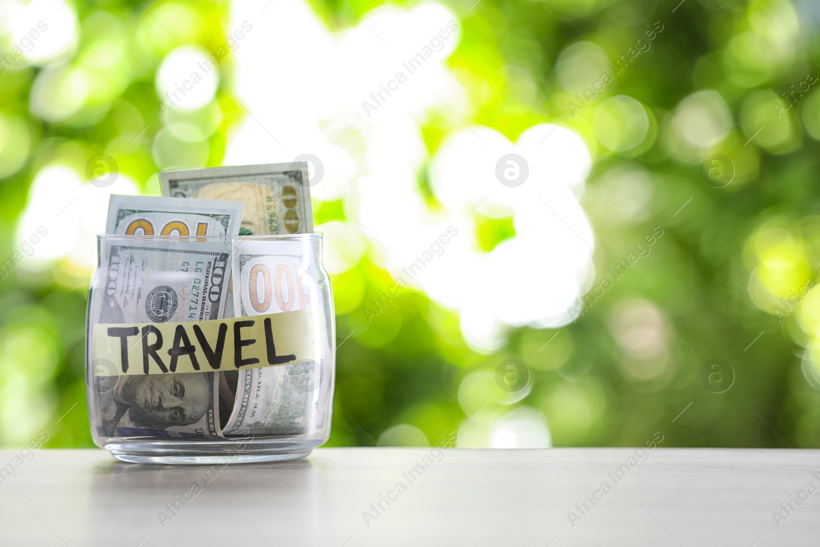 Photo of Glass jar with money and label TRAVEL on table against blurred background. Space for text
