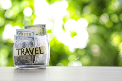 Glass jar with money and label TRAVEL on table against blurred background. Space for text