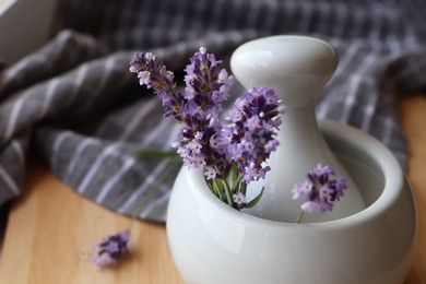 Mortar with fresh lavender flowers and pestle on table, closeup