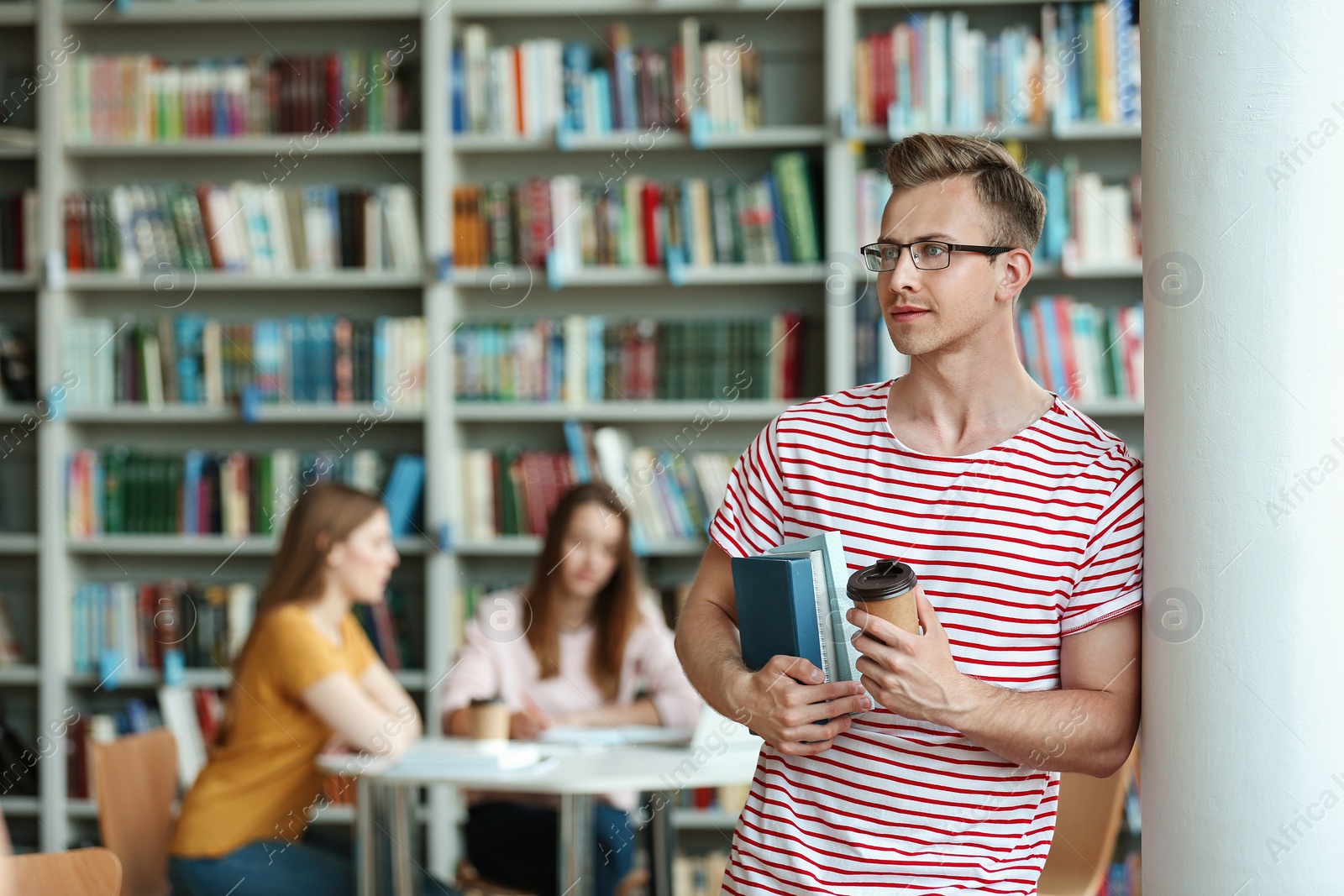 Photo of Young man with books and drink in library. Space for text