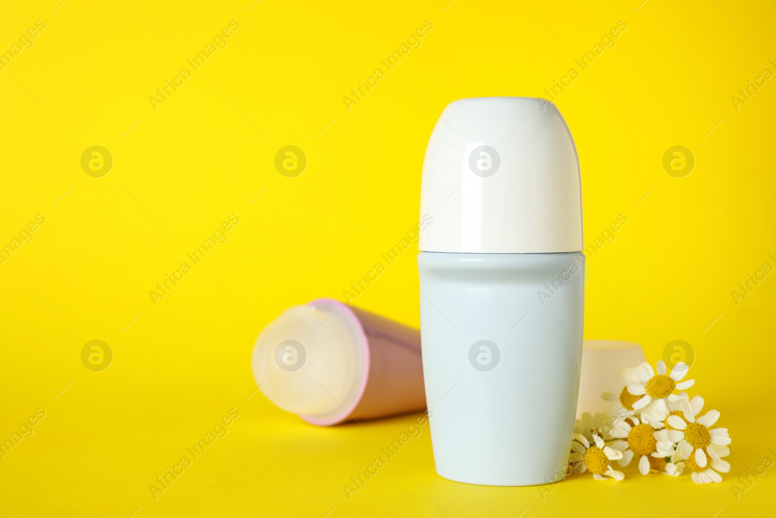 Photo of Female roll-on deodorants and chamomile flowers on yellow background, space for text