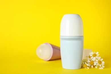 Photo of Female roll-on deodorants and chamomile flowers on yellow background, space for text