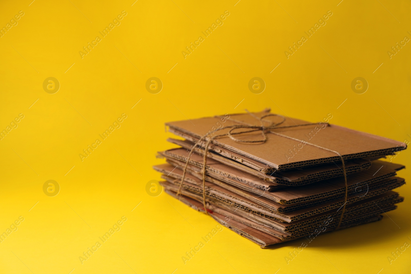 Photo of Waste paper tied with twine on yellow background, space for text