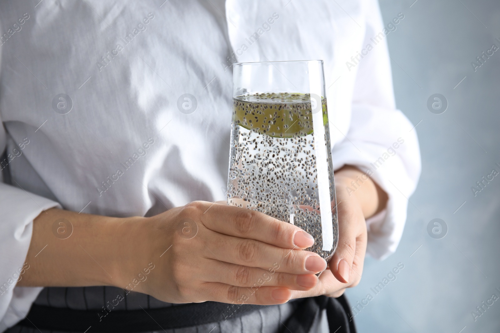 Photo of Woman holding glass of water with chia seeds on color background, closeup