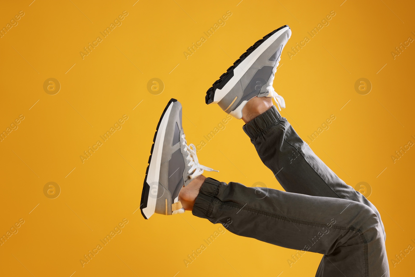 Photo of Man wearing stylish sneakers on yellow background, closeup. Space for text