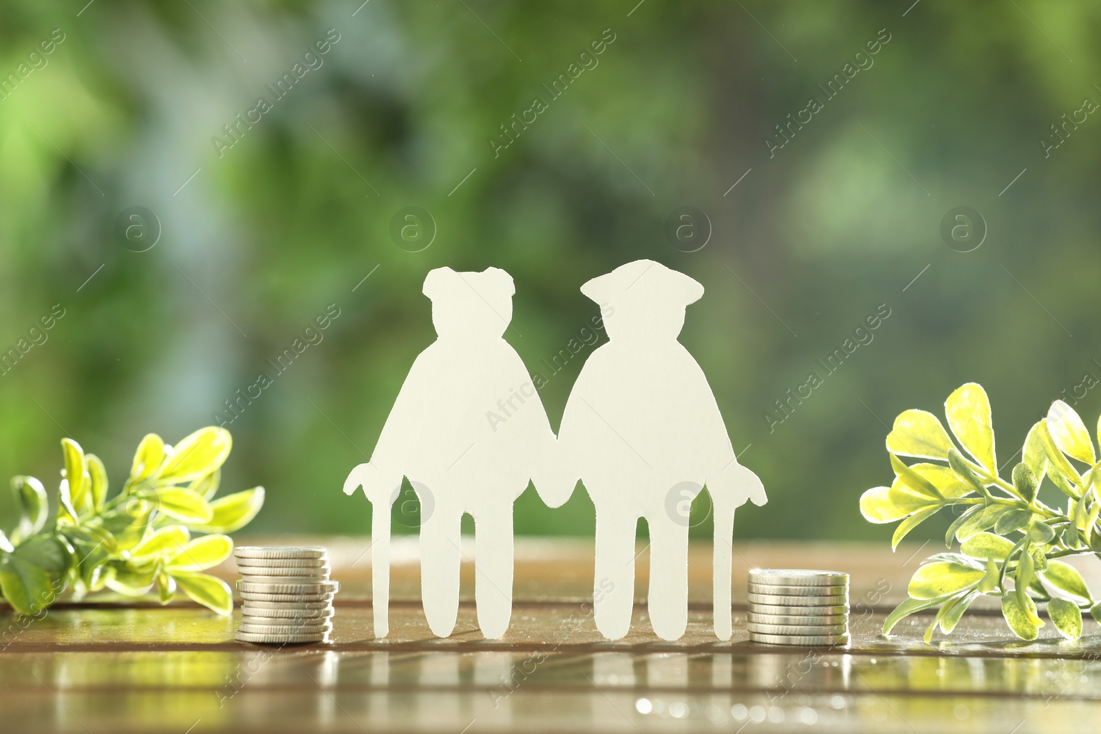 Photo of Pension savings. Figure of senior couple, stacked coins and green twigs on wooden table outdoors