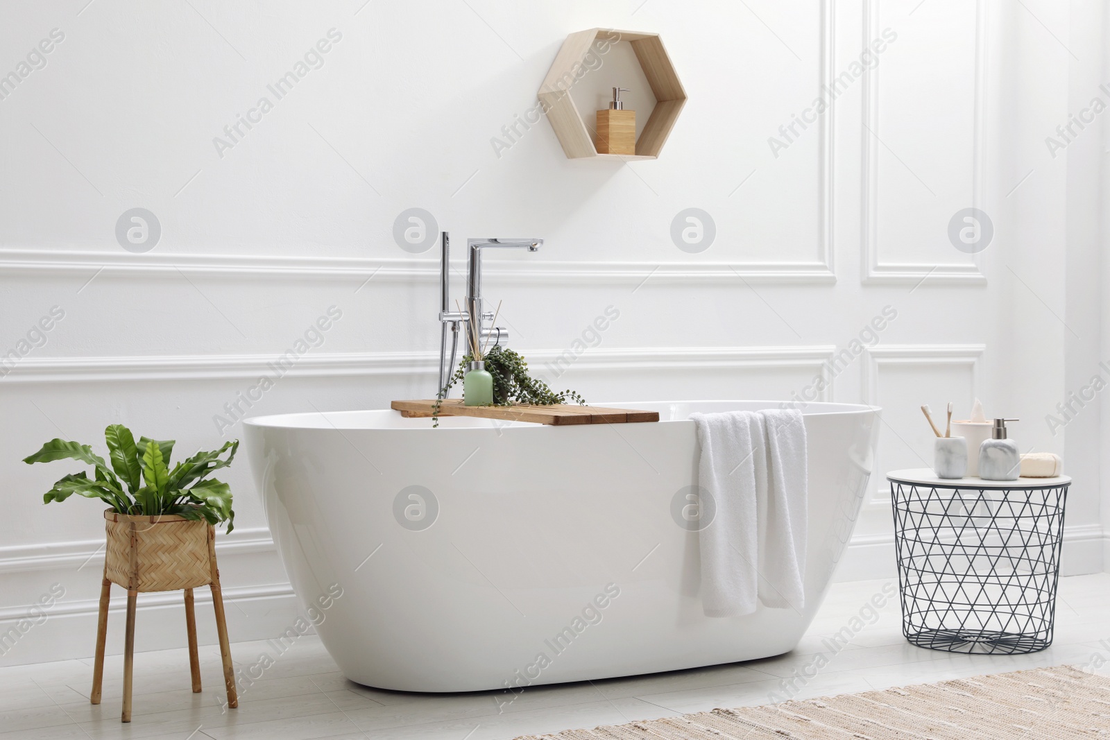 Photo of Modern ceramic bathtub and green plants near white wall in room